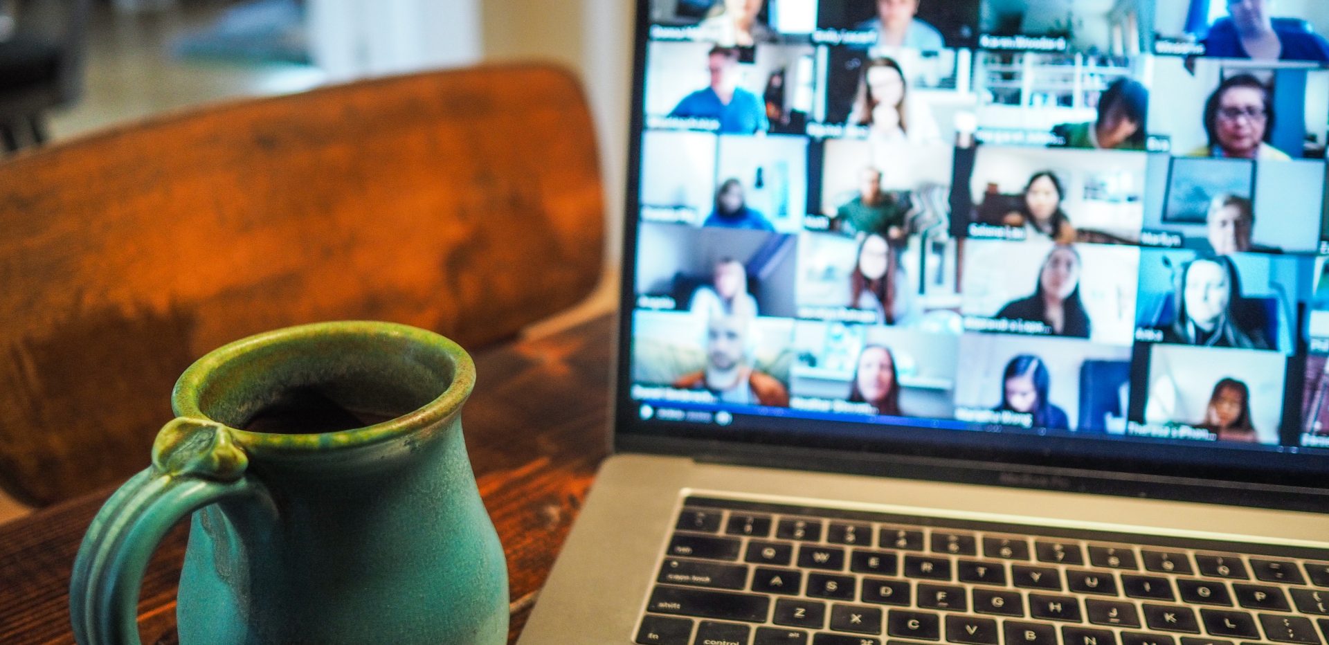 En kaffekop er stillet ved siden af en computer med en videomøde på skærmen. 