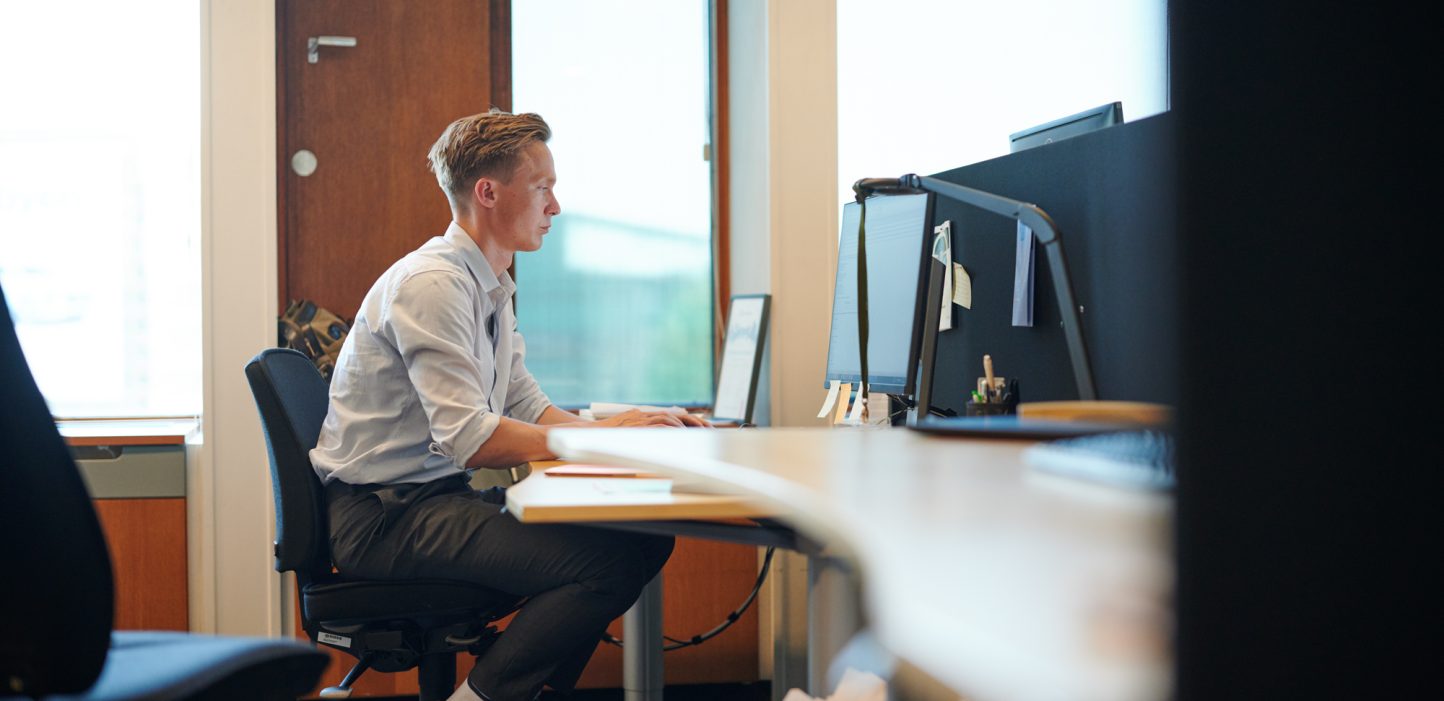Kontormiljø hvor person sidder ved computer. 